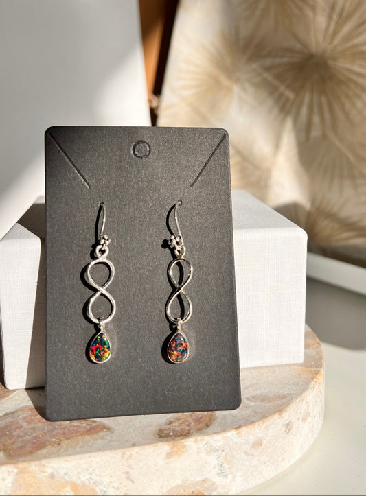 Pair of silver earrings with colorful opal stones on a black card against a neutral background